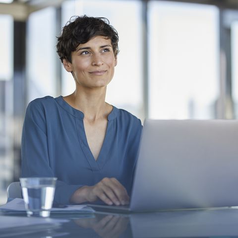 smiling businesswoman sitting at desk in office with laptop