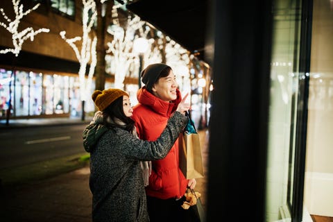 Smiling couple admiring items in widow while holiday shopping on winter evening Smiling couple admiring items in widow while holiday shopping on winter evening