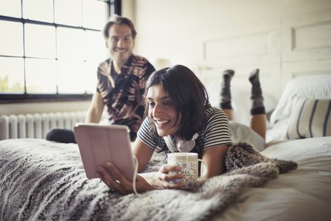 Smiling couple relaxing, drinking coffee and using digital tablet on bed