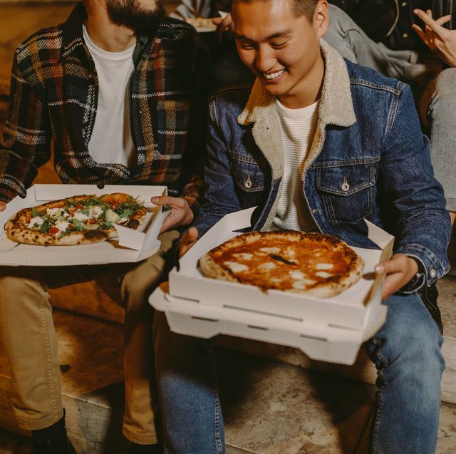 smiling friends eating pizza while sitting on steps outdoors at night