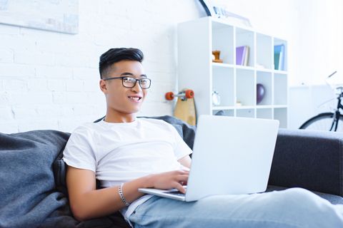 smiling handsome asian man using laptop on sofa at home
