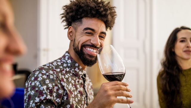 smiling man drinking red wine during dinner party at home