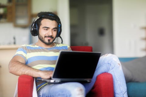 Smiling man sitting in an armchair listening to music while working on his laptop computer