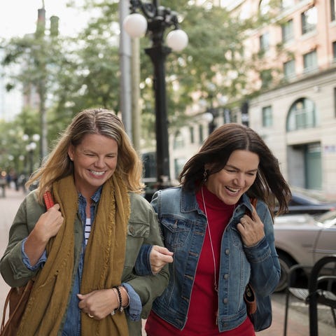 Smiling mature women friends walking arm in arm on urban sidewalk