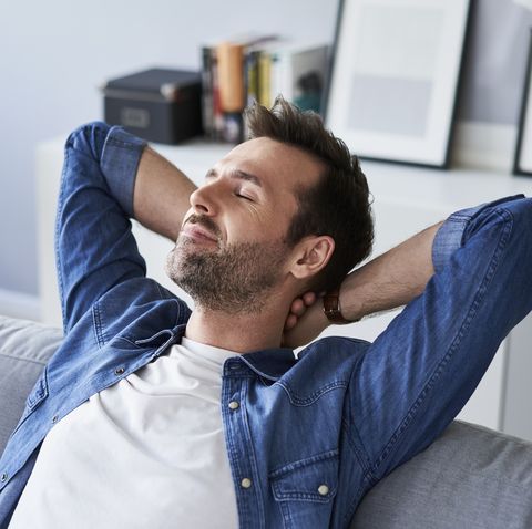 Smiling relaxed man sitting on sofa daydreaming