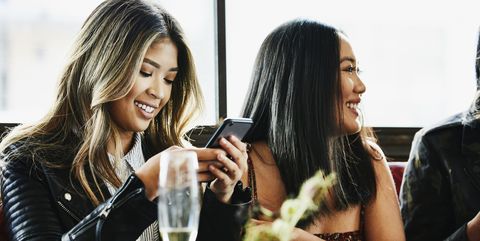 Smiling woman looking at smartphone while having lunch in restaurant with girl friends