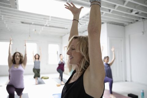 Smiling woman practicing yoga warrior one pose in yoga class