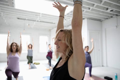 Smiling woman practicing yoga warrior one pose in yoga class Smiling woman practicing yoga warrior one pose in yoga class