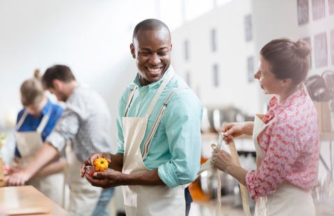 Smiling woman tying apron for man in cooking class kitchen Smiling woman tying apron for man in cooking class kitchen