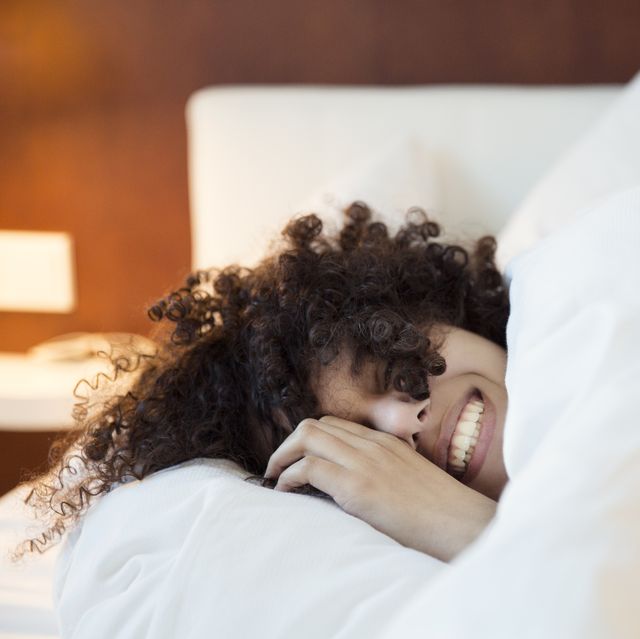 best bamboo sheets  a smiling woman with dark curly hair in bed under the covers, head on a white pillow