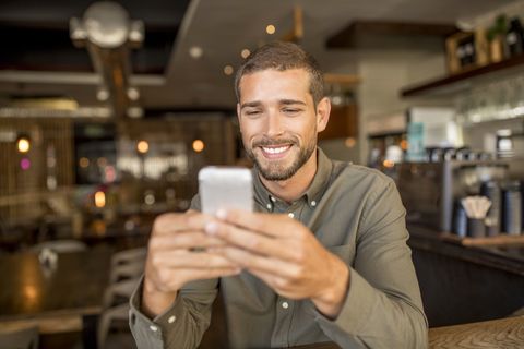 Smiling young man using smartphone in a cafe