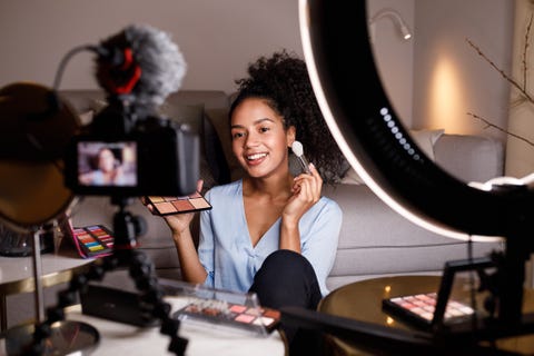 smiling young woman applying make up while being filmed in camera