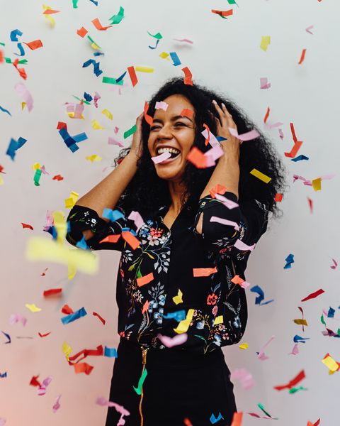 smiling young woman standing amidst confetti against wall