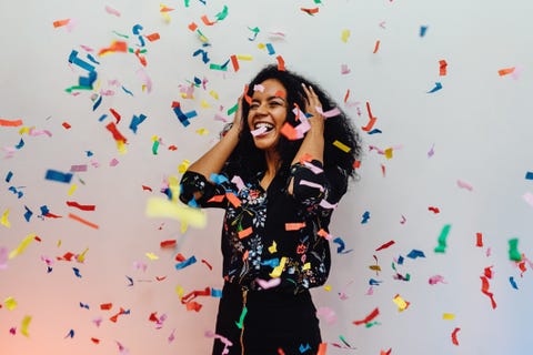 smiling young woman standing amidst confetti against wall