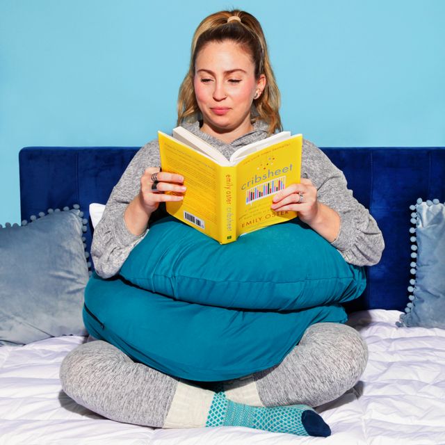 woman sitting upright and reading with snoogle pregnancy pillow