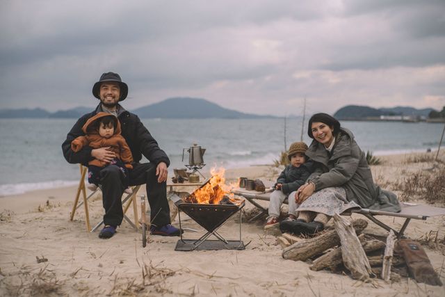 family sitting by fire by the beach