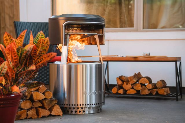 a solo stove pi fire pizza oven on a patio next to chopped wood and a potted plant