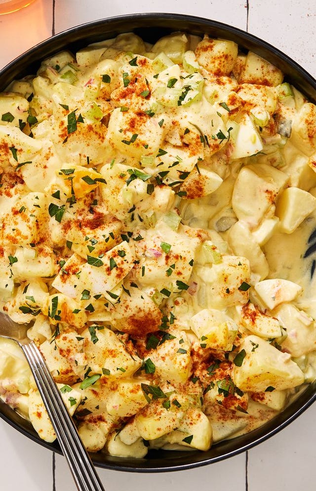 southern potato salad topped with paprika and chopped parsley in a black bowl on a white tile background