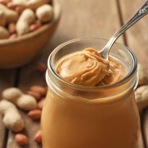 Spoon and glass jar with creamy peanut butter on kitchen table, closeup