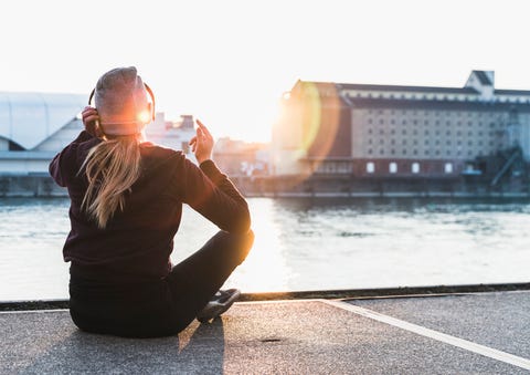 Sportive young woman having a break at the riverside in the city at sunset