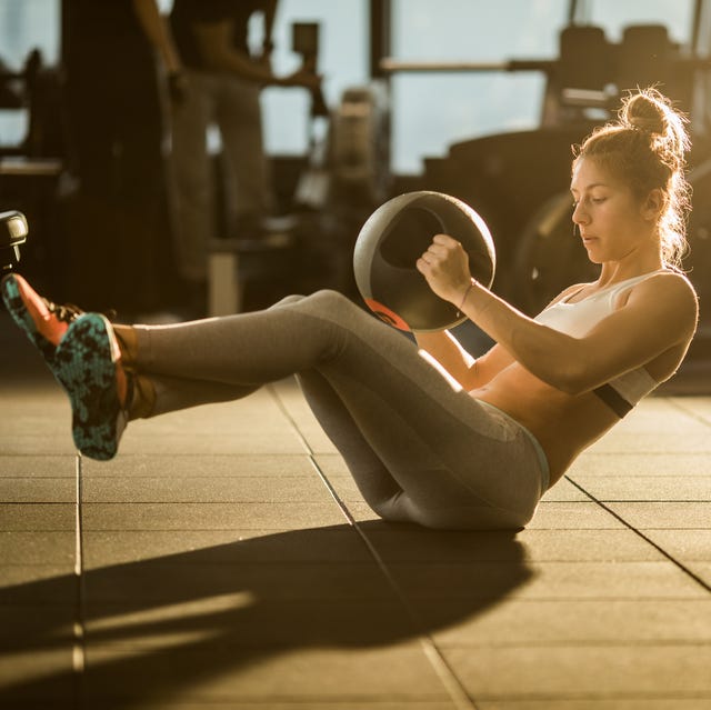 Sportswoman doing sit-ups with medicine ball on sports training in a gym.