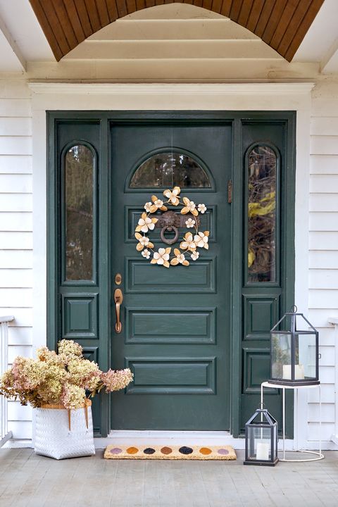green front door with gold wreath multicolor doormat flowers next to door