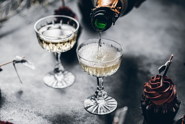 close up of pouring champagne in a glasses over black table with cup cake serving drinks for new years party