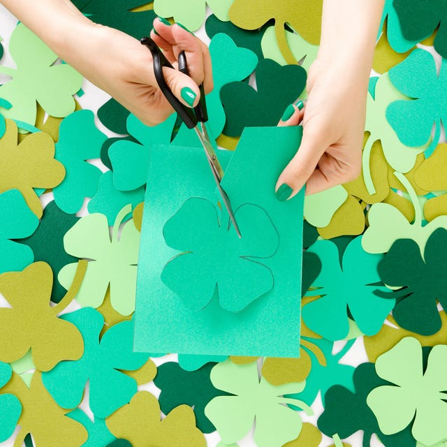 young woman cutting green paper clovers