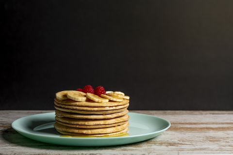 stack of pancakes with honey, bananas and raspberries