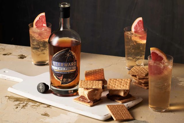 a bottle of starward whiskey on a table with cocktails and smores