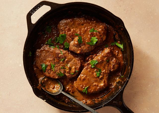 three beef tenderloin steaks covered in creamy brown sauce and chopped parsley in a cast iron pan with a spoon sticking out of it