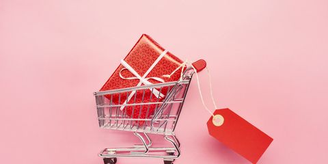 still life of a small shopping cart with red gift and blank price tag on pink colored background