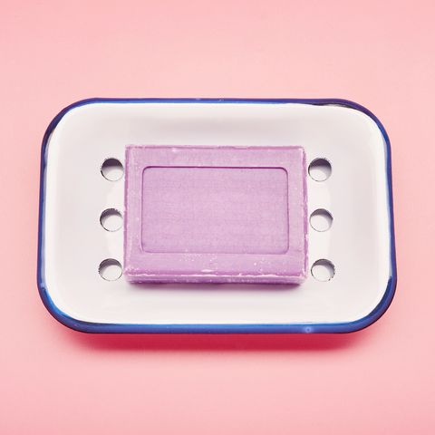 Still life of an enamel soap dish and bar soap for washing hands on pink background