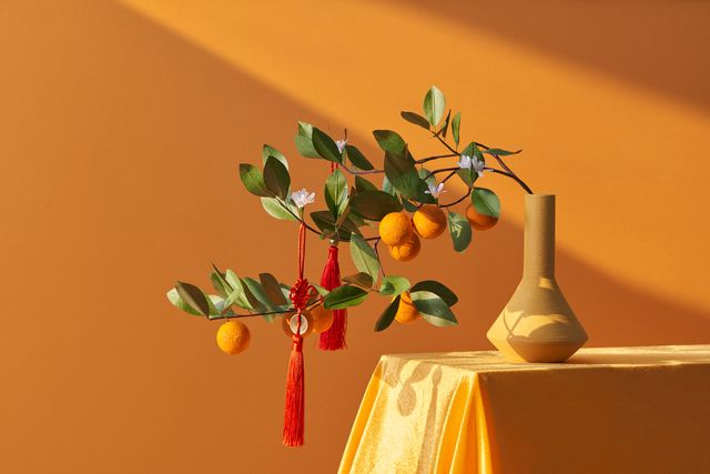 vase on a table with mandarin branches and red chinese new year decor hanging off the branches