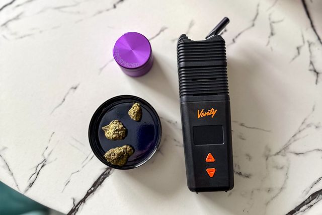a black vape and a purple grinder with buds of weed on a table
