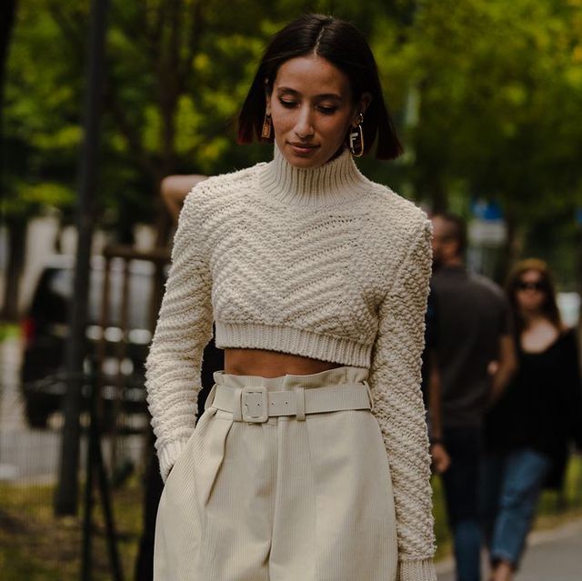 a woman walks through paris during fashion week wearing a cropped cable knit sweater and trousers with a paperbag waist