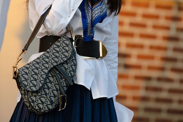 a woman stands outside on her cell phone at new york fashion week carrying a dior saddle bag to illustrate a roundup of the best vintage consignment websites 2022
