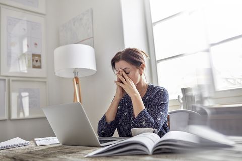 Stressed woman cradling face in hands while sitting behind computer.