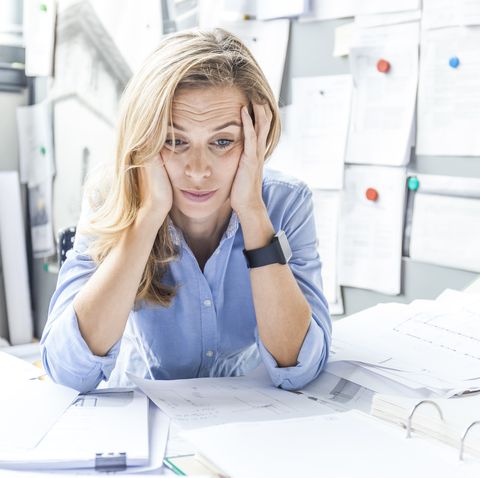 stressed woman sitting at desk in office surrounded by paperwork
