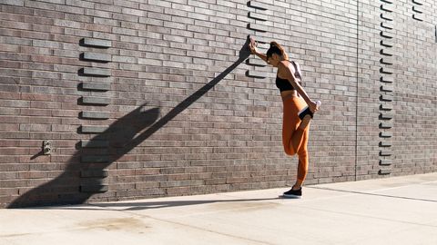 Mujer estirando piernas en un muro