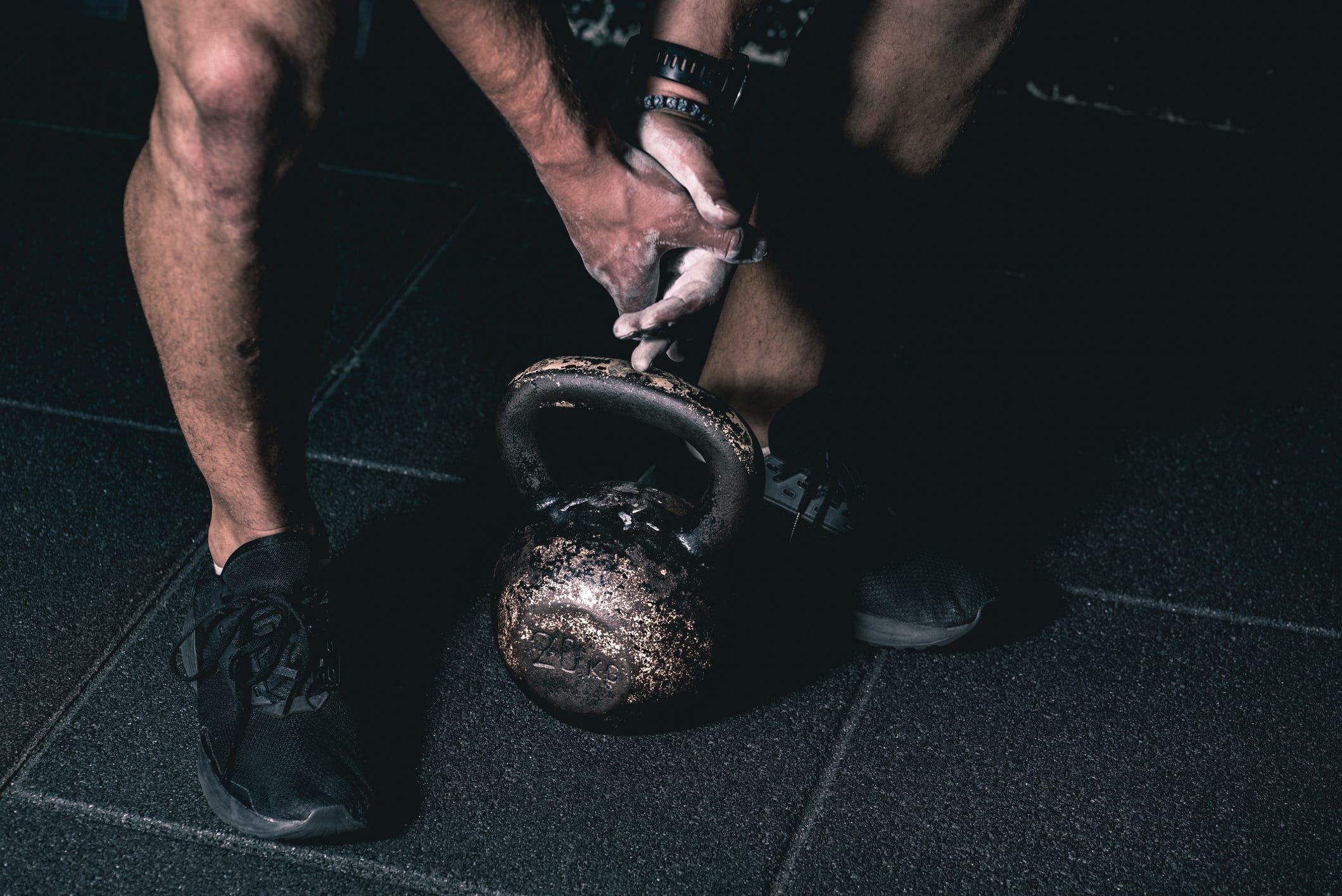 Sterk gespierde man die met zijn hand een zware rode kettlebell vasthoudt op de vloer van de sportschool, klaar voor een cross strength and conditioning training en workout