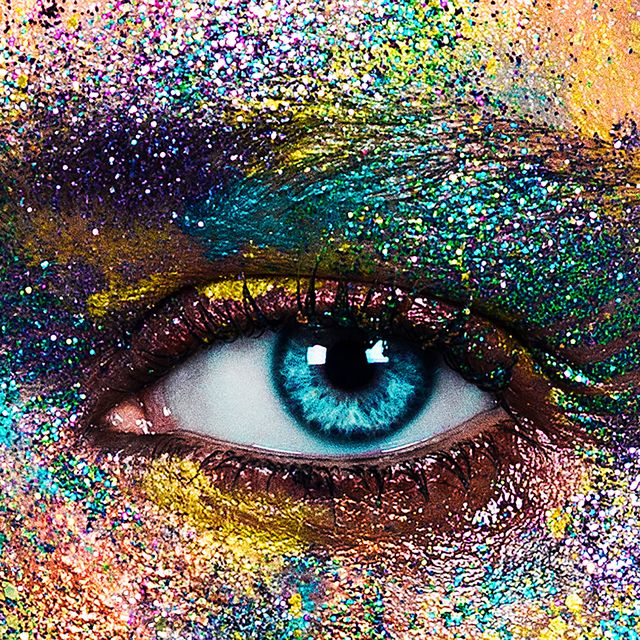 studio portrait of blue eyed young woman with glittery multi coloured powder on face, close up of eye