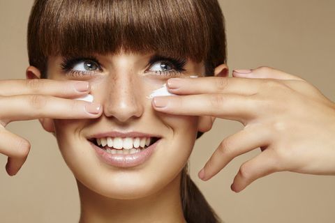 studio shot of a young brunette applying cream on her face