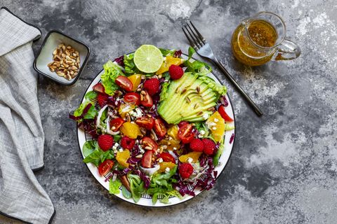 studio shot of fruity salad plate with lambs lettuce, radicchio, lettuce hearts, avocado, tomato, pine nuts, raspberries, oranges, lime
