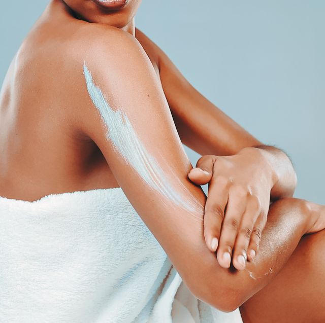 studio shot of woman wrapped in towel applying body lotion