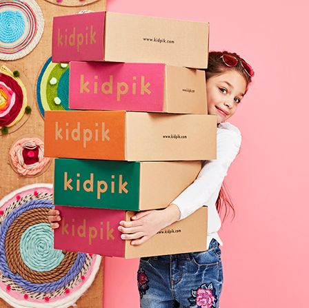 girl holding multiple monthly clothing subscription boxes from kidpik on the left and rainbow cupcake on the right