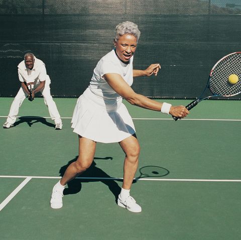senior woman hitting a tennis ball on a tennis court and a senior man standing behind on a summer date