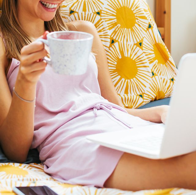 woman laying in bed with laptop and coffee mug in pajamas