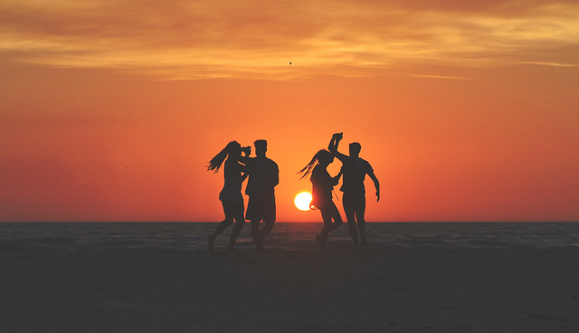 four people dancing on a beach with a sunset in the background