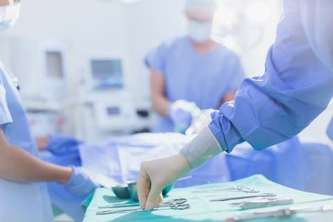 Surgeon in rubber gloves reaching for surgical scissors on tray in operating room Surgeon in rubber gloves reaching for surgical scissors on tray in operating room